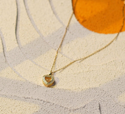 A delicate gold necklace with a small textured gold pendant is draped over a modern abstract wall art piece featuring beige, gray, and orange shapes.