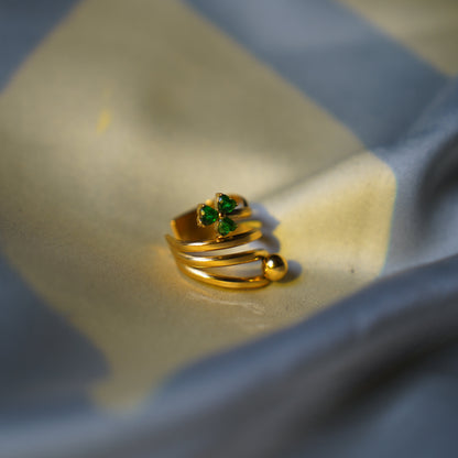 A gold-plated wrap ring with a small green gemstone accent, resting on a draped blue and beige fabric surface.